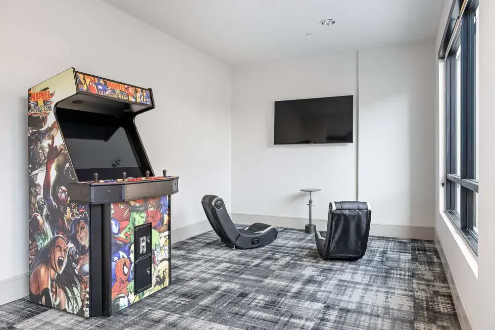 Arcade game room with an arcade cabinet, TV, gaming chairs, and patterned carpet.