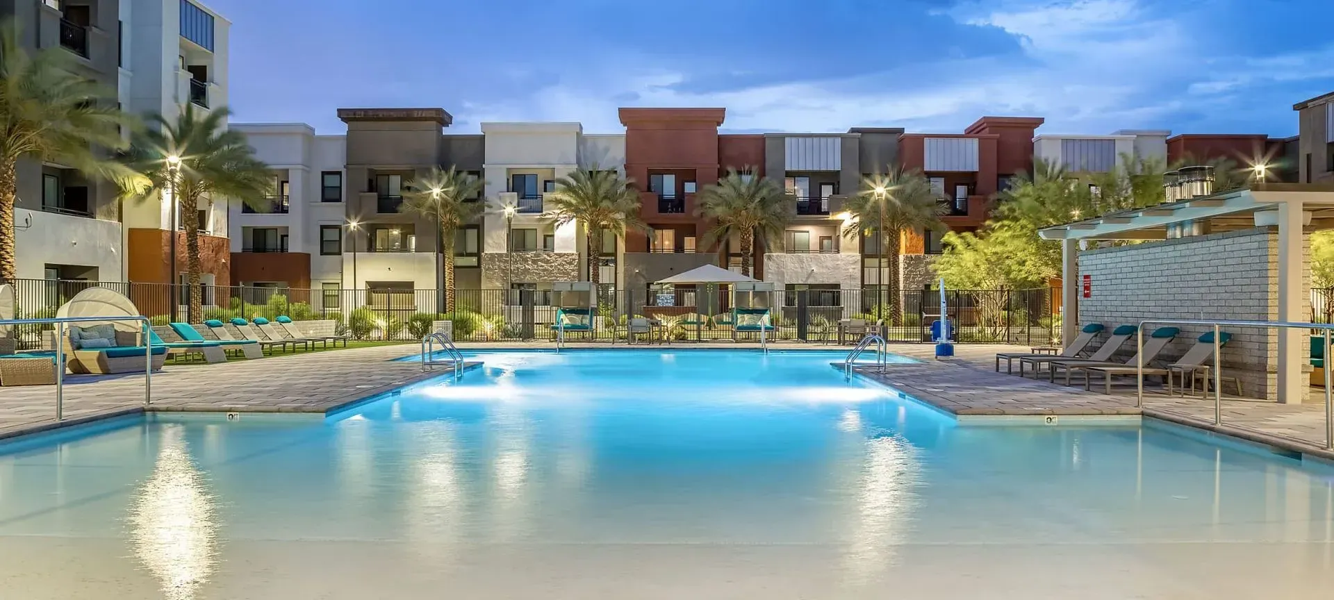A large swimming pool in front of a modern apartment complex at dusk.
