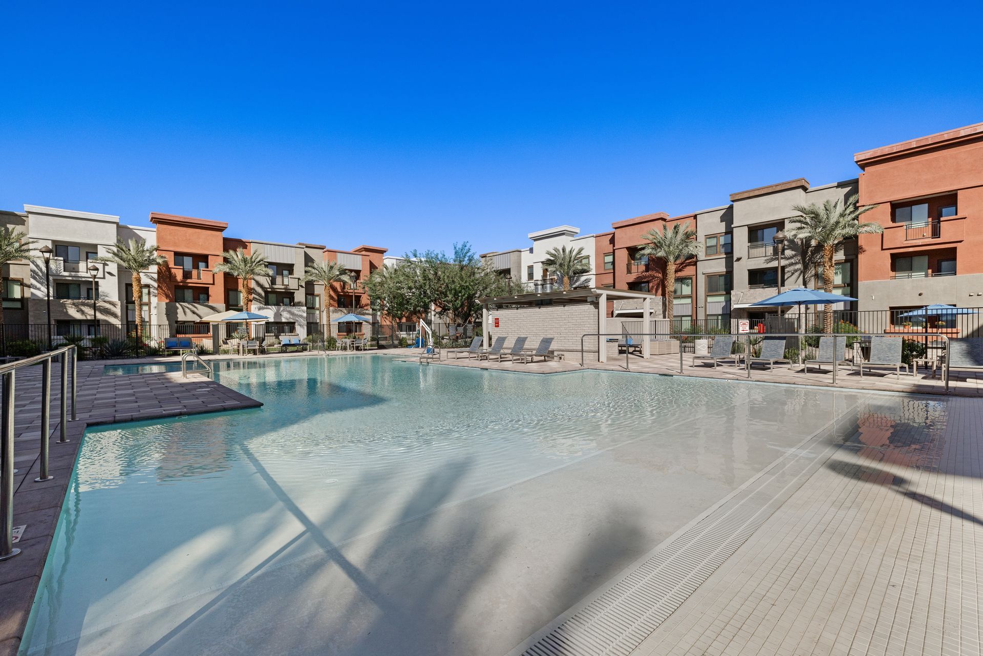 Modern apartment complex pool with clear water and lounge chairs under a blue sky