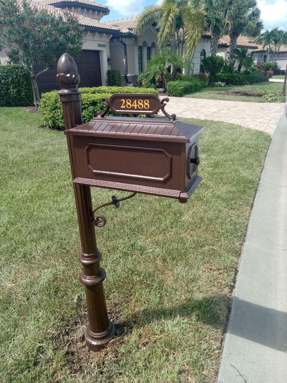A brown mailbox is sitting in the grass in front of a house.