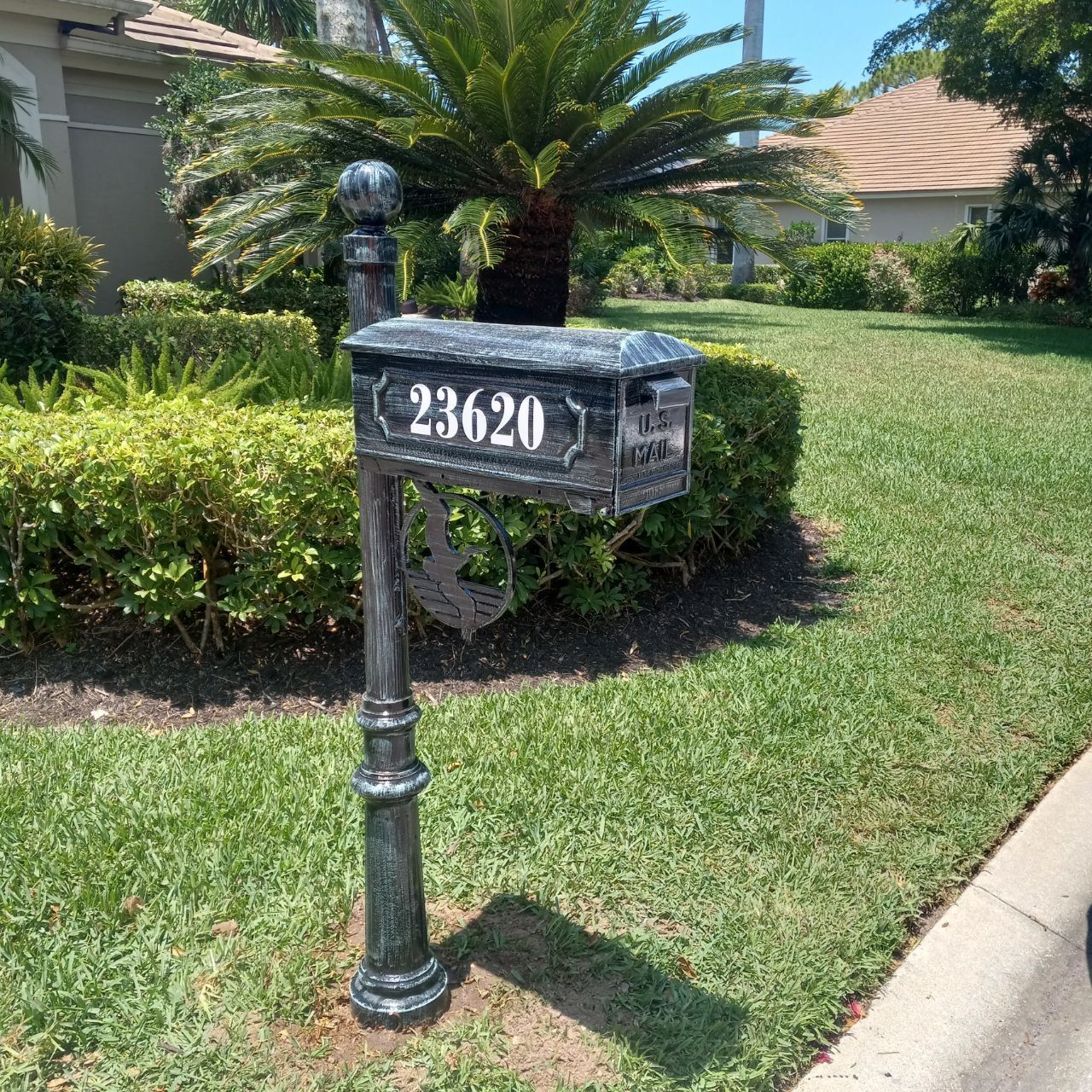 A black mailbox is sitting in the grass in front of a house.