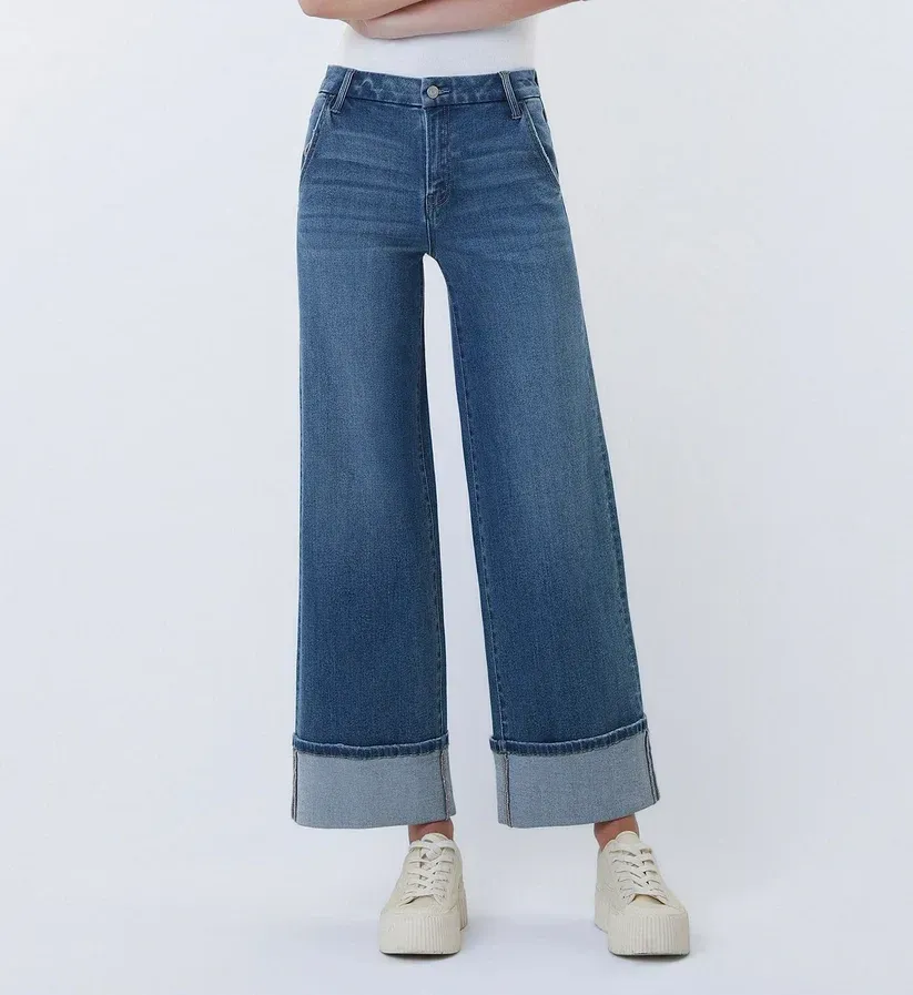 Blue wide-leg jeans with rolled cuffs and white sneakers on a plain background