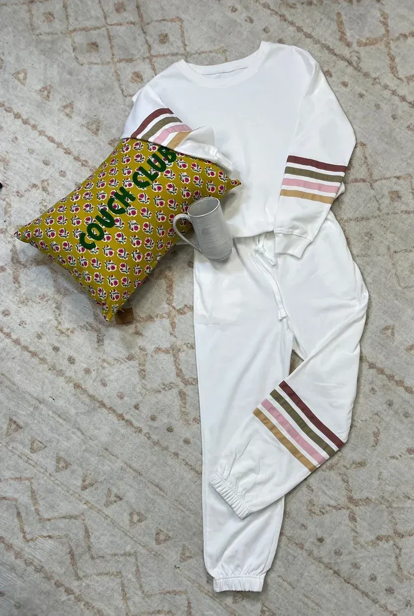 White casual outfit with striped sleeves and pant legs, laid beside a patterned bag on a tiled floor