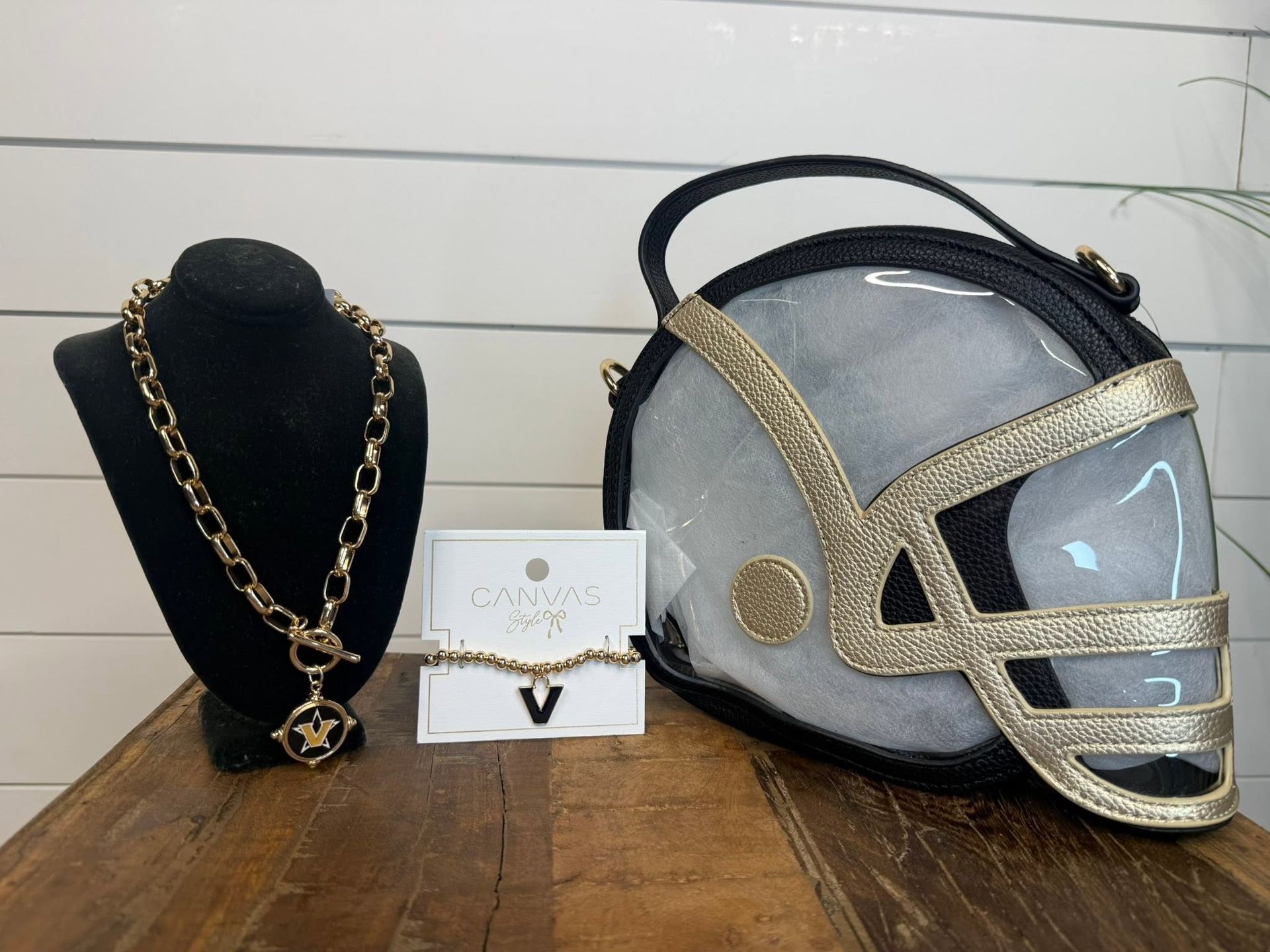 Gold necklace on black display bust beside earrings and black-and-gold purse on wood table