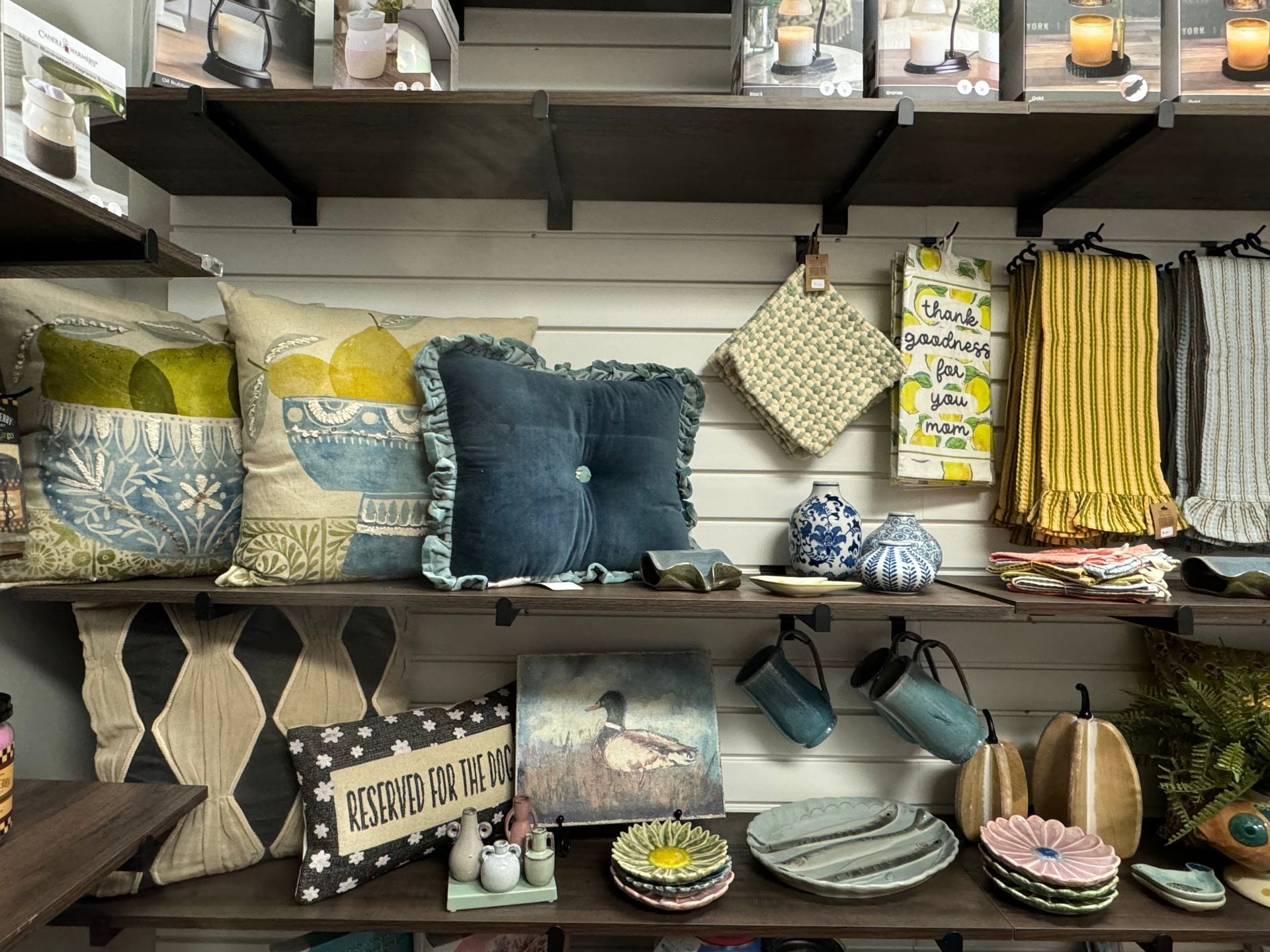 Colorful handmade pillows and decor displayed on a store shelf, including blue, cream, and floral patterns.