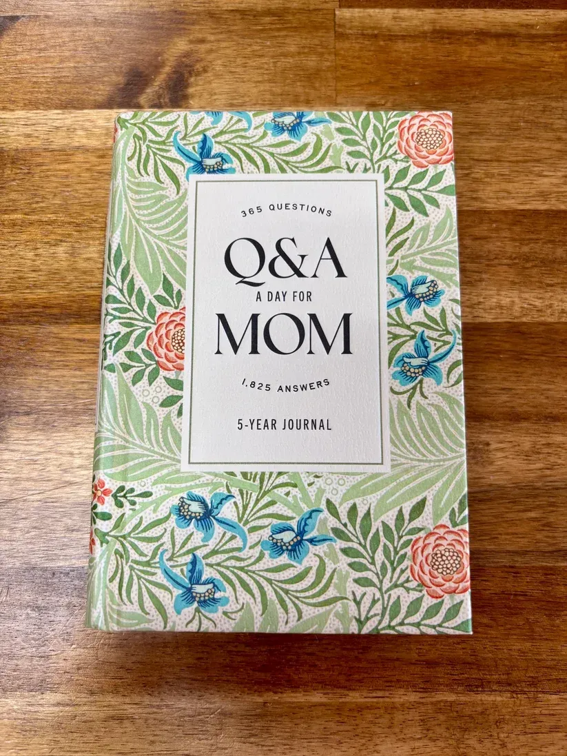 Floral-patterned book cover with the title “Q&A for Mom” on a wooden table