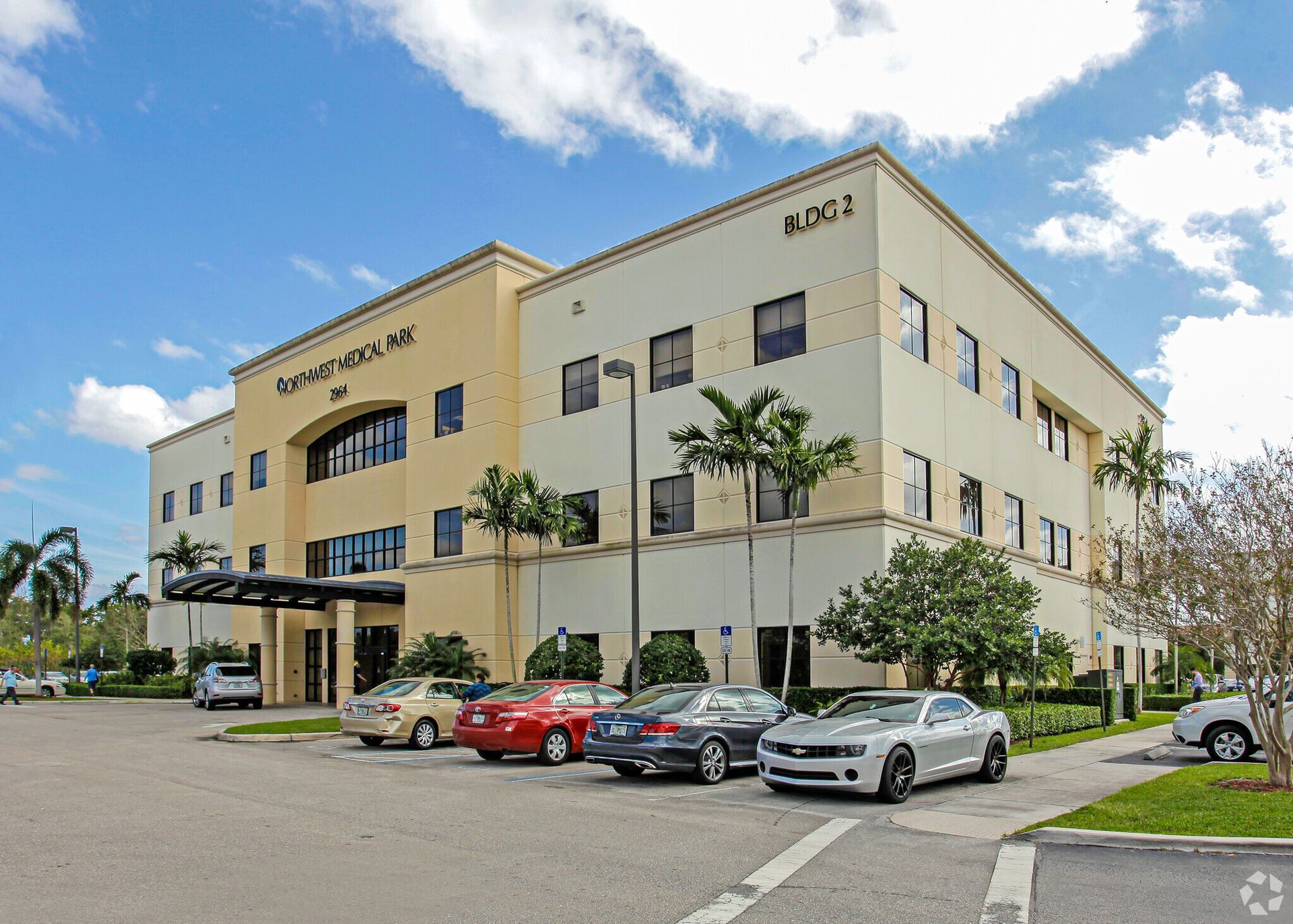 Three-story beige office building with parked cars in front under a blue sky