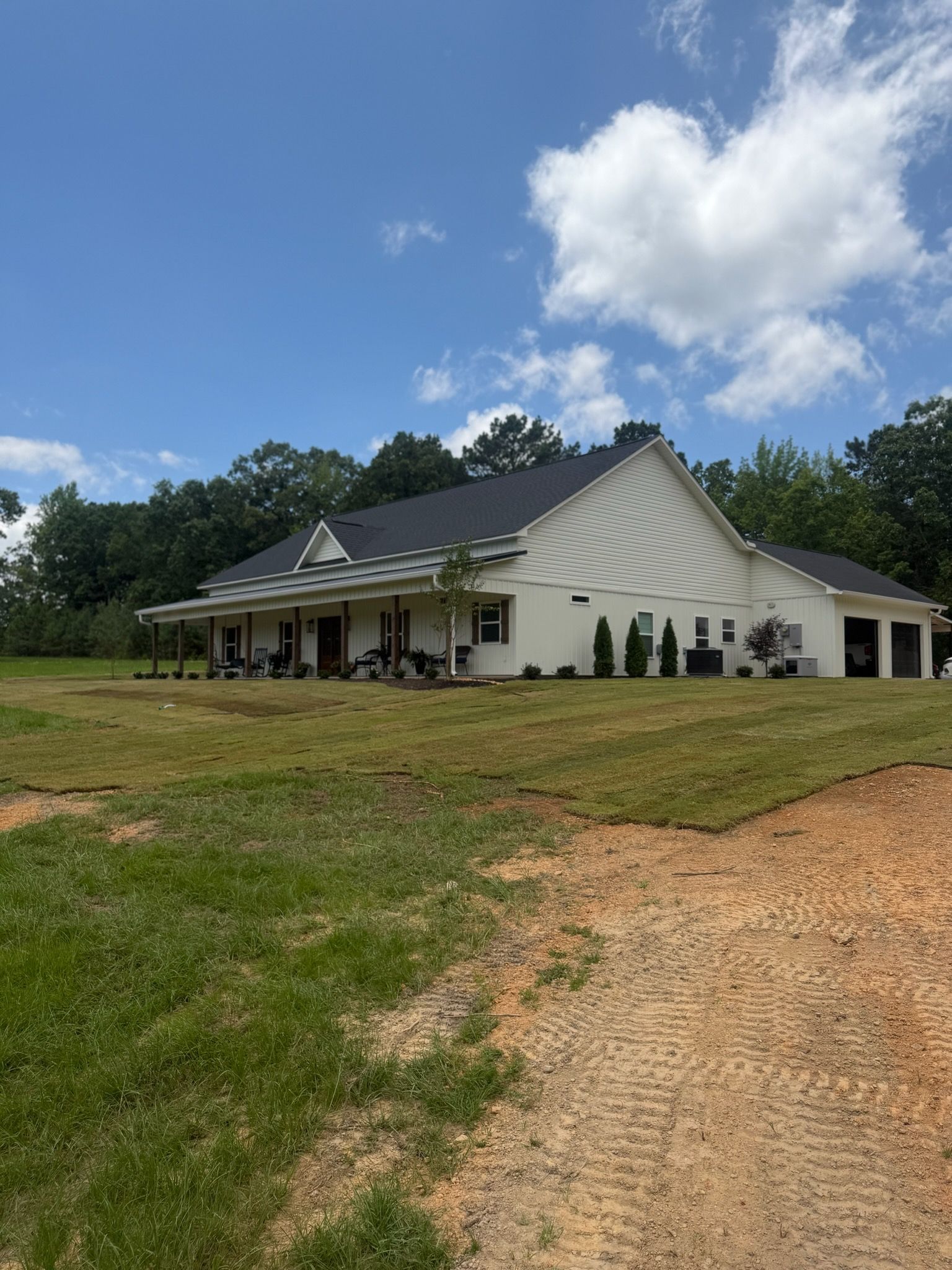 White house with dark roof on a grassy lot under a bright blue sky with clouds