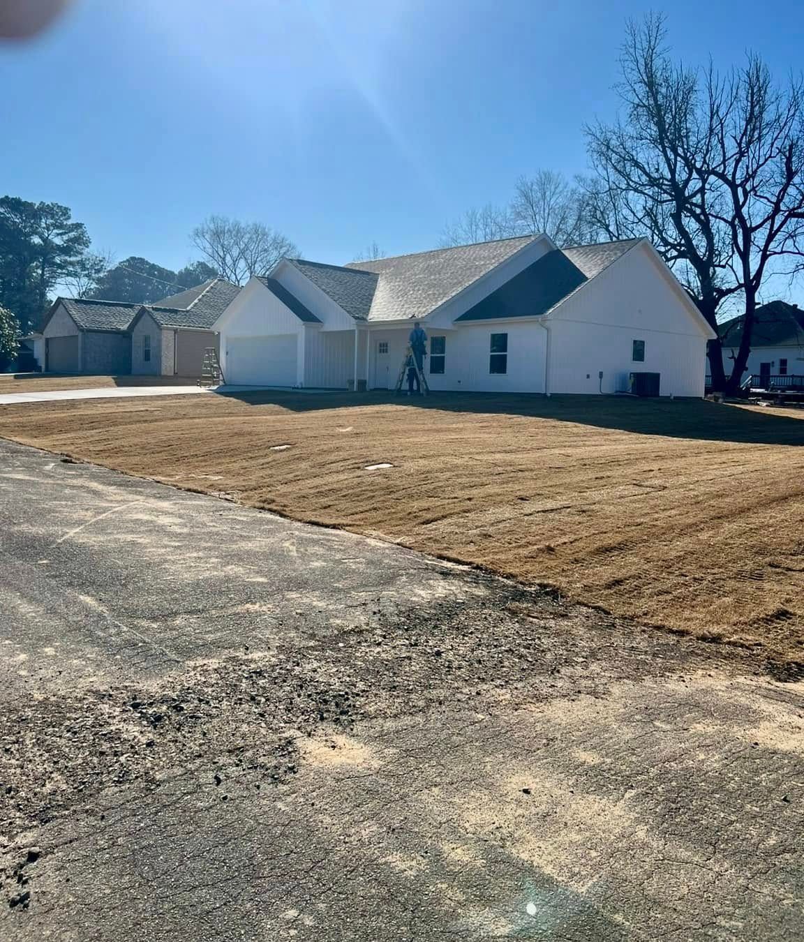 White suburban houses with a large brown lawn and a gravel driveway under a clear blue sky.