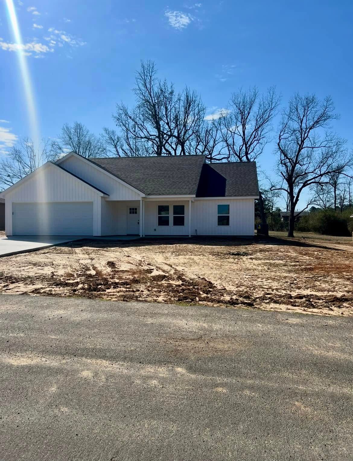 Single-story white house with a garage and bare trees under a bright blue sky