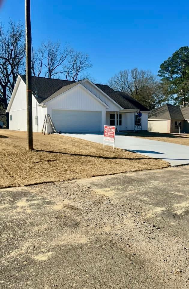 Suburban house with two-car garage, new concrete driveway, and a yard sign by the road.