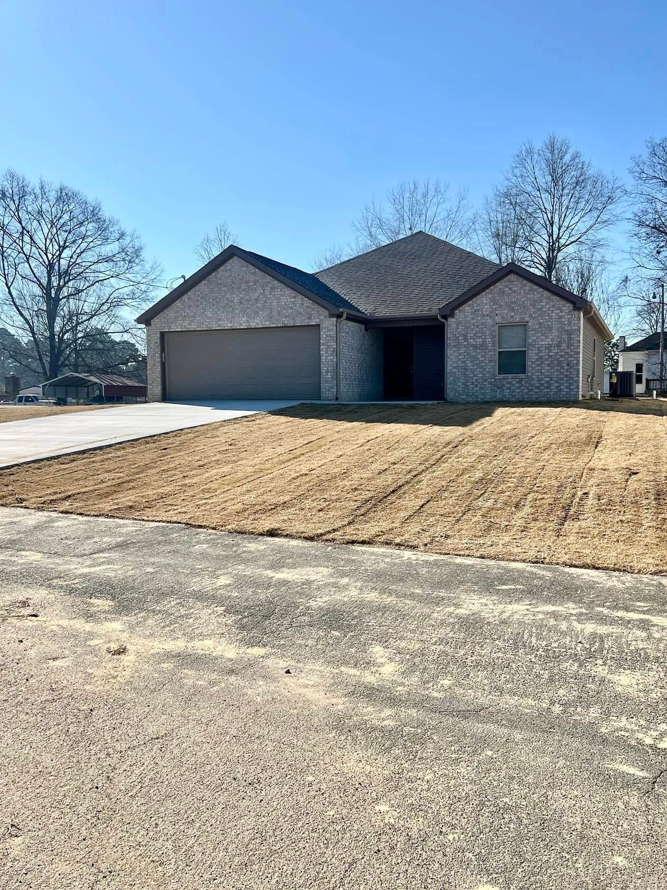 Single-story brick house with a two-car garage and bare front lawn on a clear day