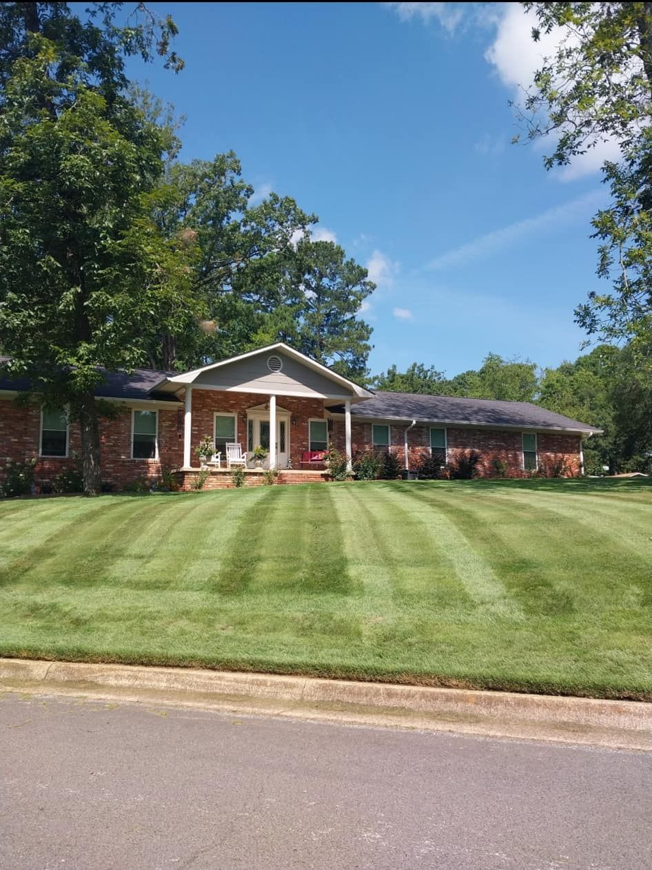 Single-story brick house with a white porch, wide green lawn, and trees under a blue sky