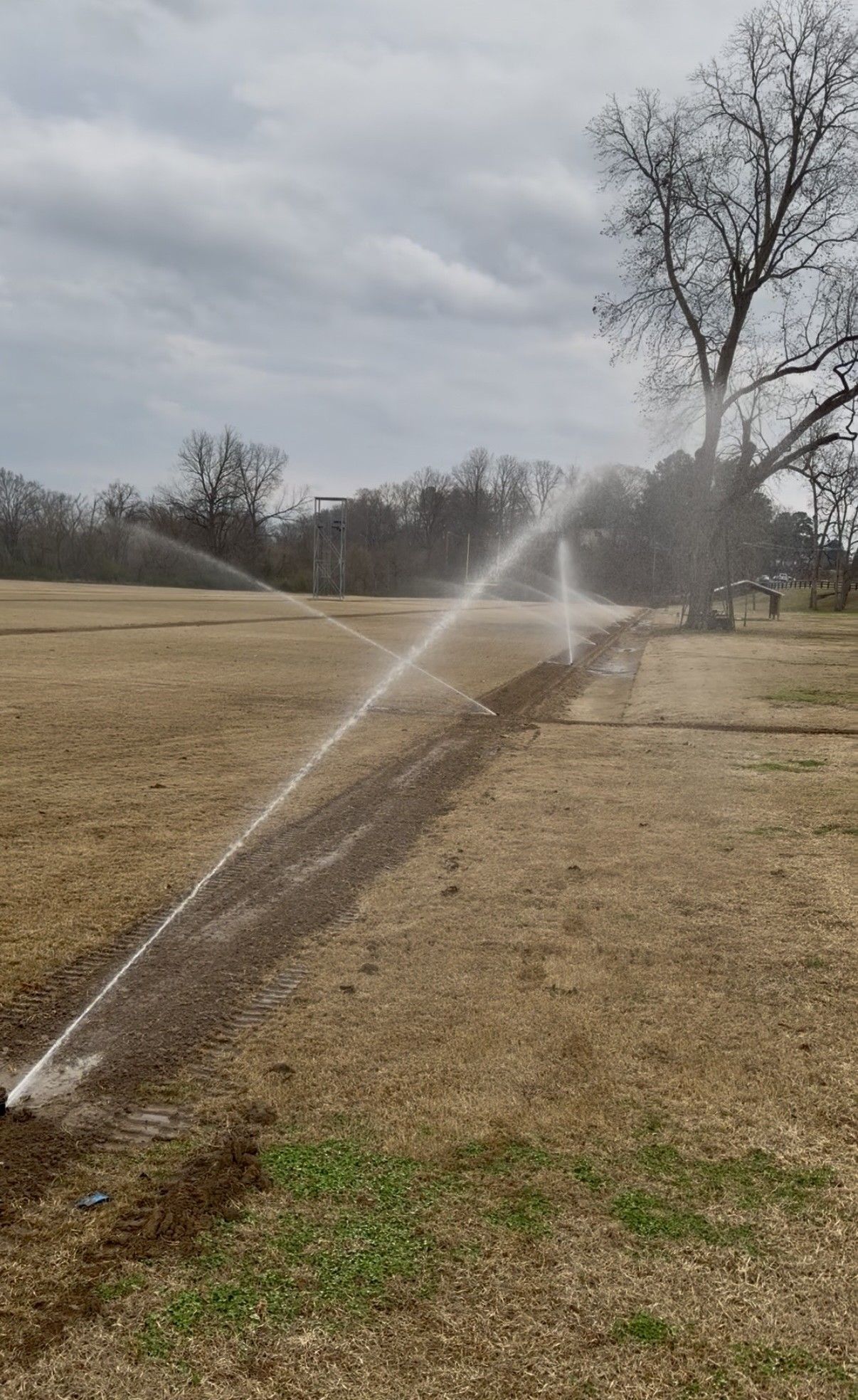 Irrigation sprinklers spraying water over a grassy field on an overcast day
