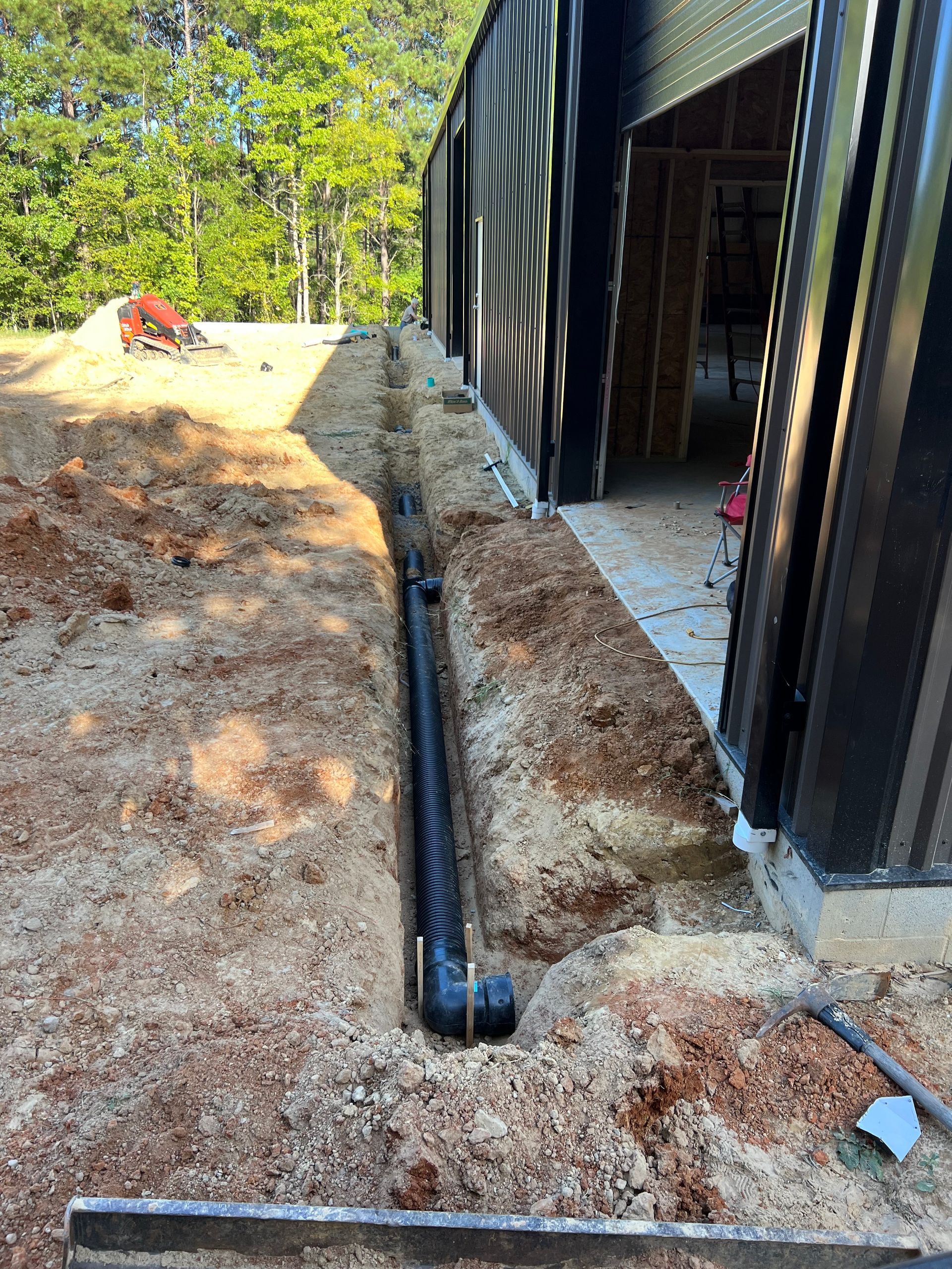 Black drainage pipe along a dirt trench beside a metal building at a construction site