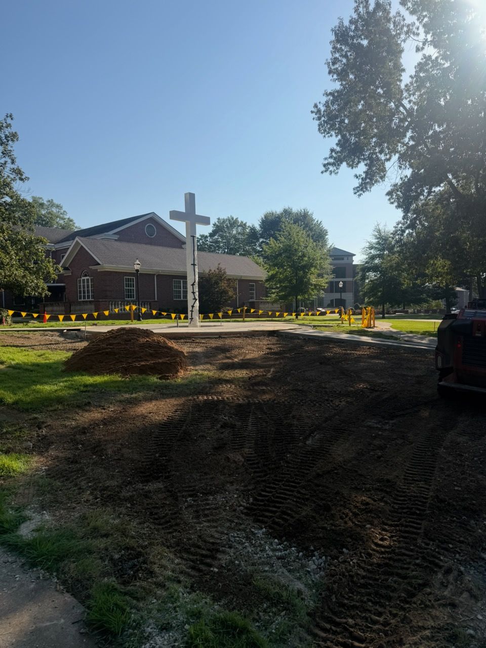 Roadwork in front of a church building with a large white cross under a bright blue sky