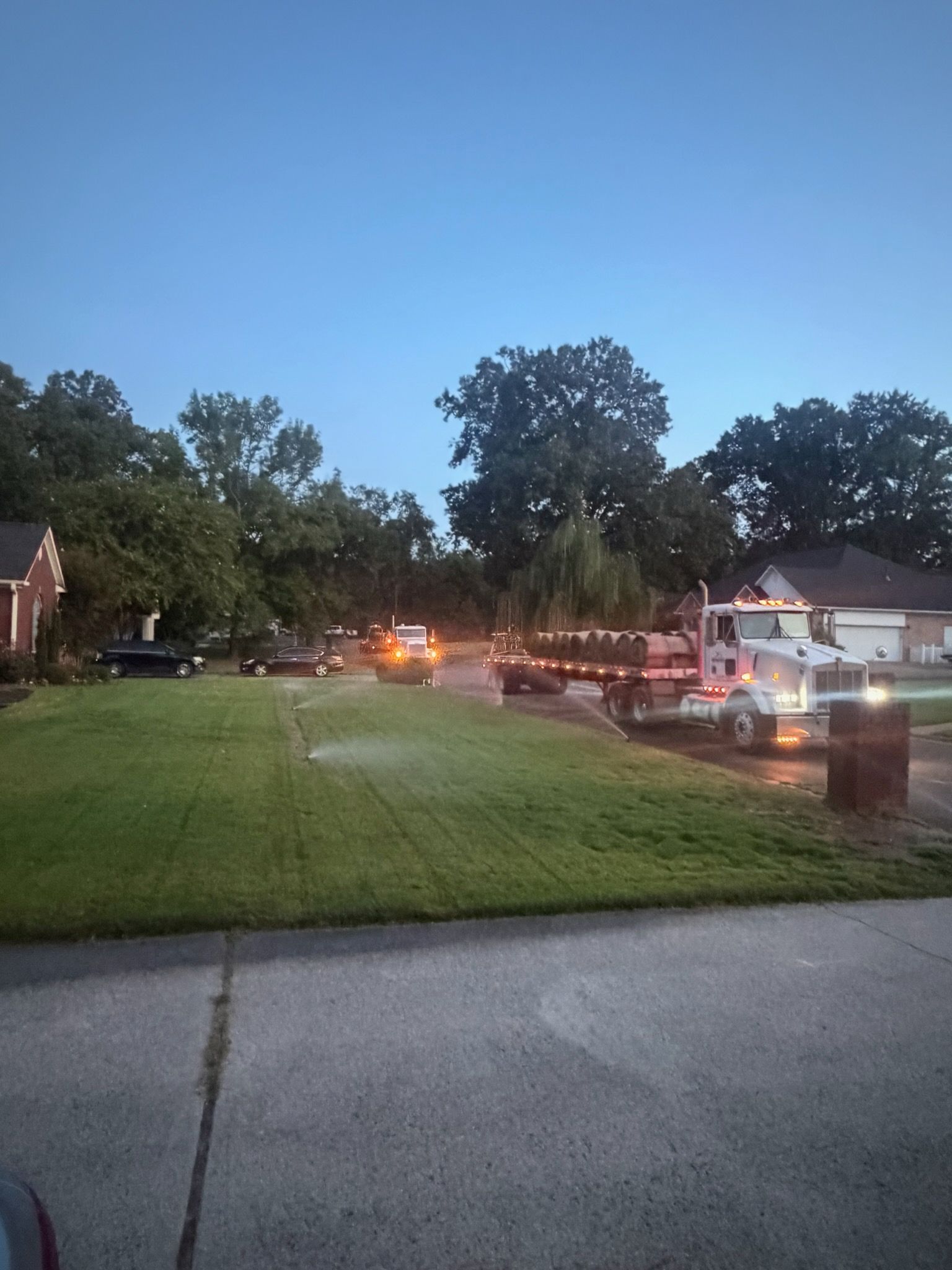 Fire trucks and emergency lights on a residential street at dusk, with firefighters near parked vehicles.