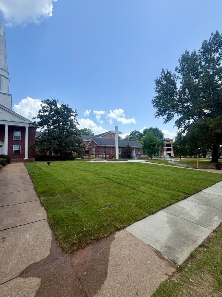 Apartment courtyard with green lawn, concrete paths, and brick buildings under a clear blue sky