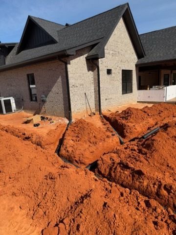 House under construction with red dirt piled around the foundation and excavated trenches in front