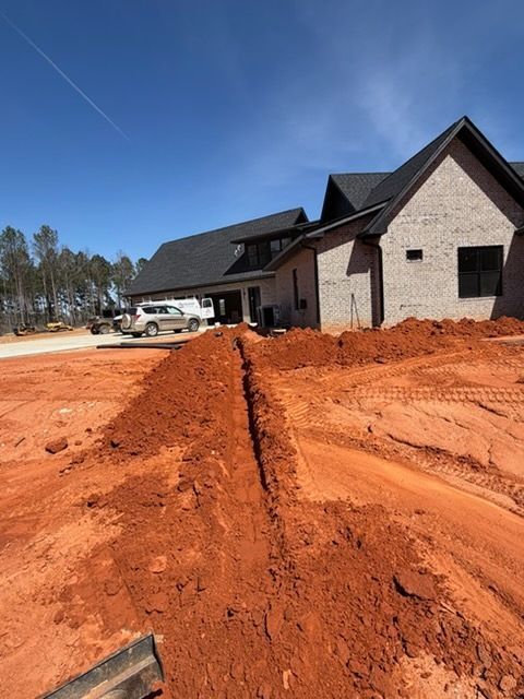 New house under construction with red dirt driveway and brick exterior under a clear blue sky