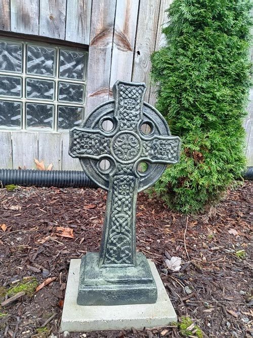 A stone cross statue in front of a wall.
