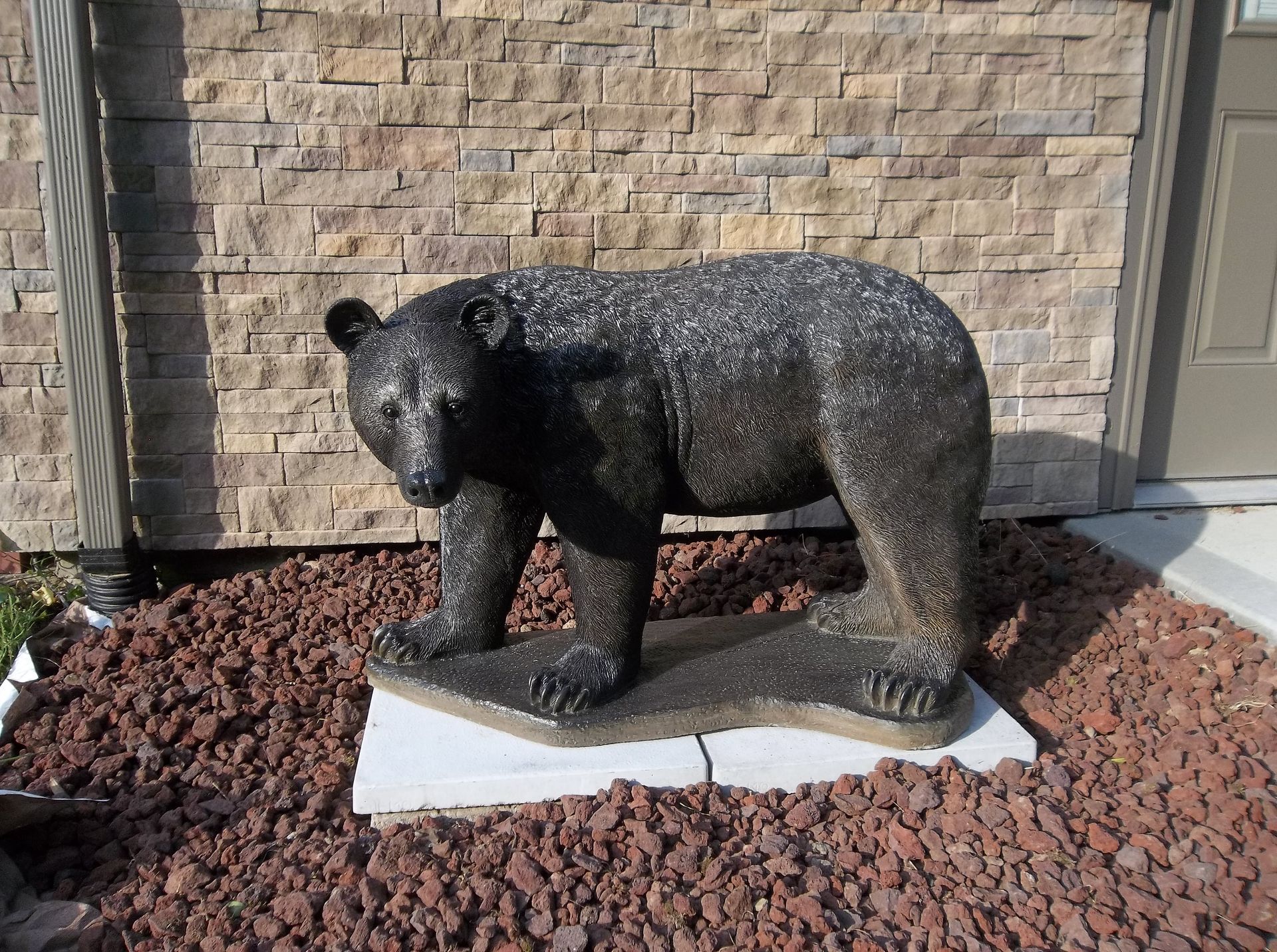 A statue of a bear standing on a rock in front of a brick wall