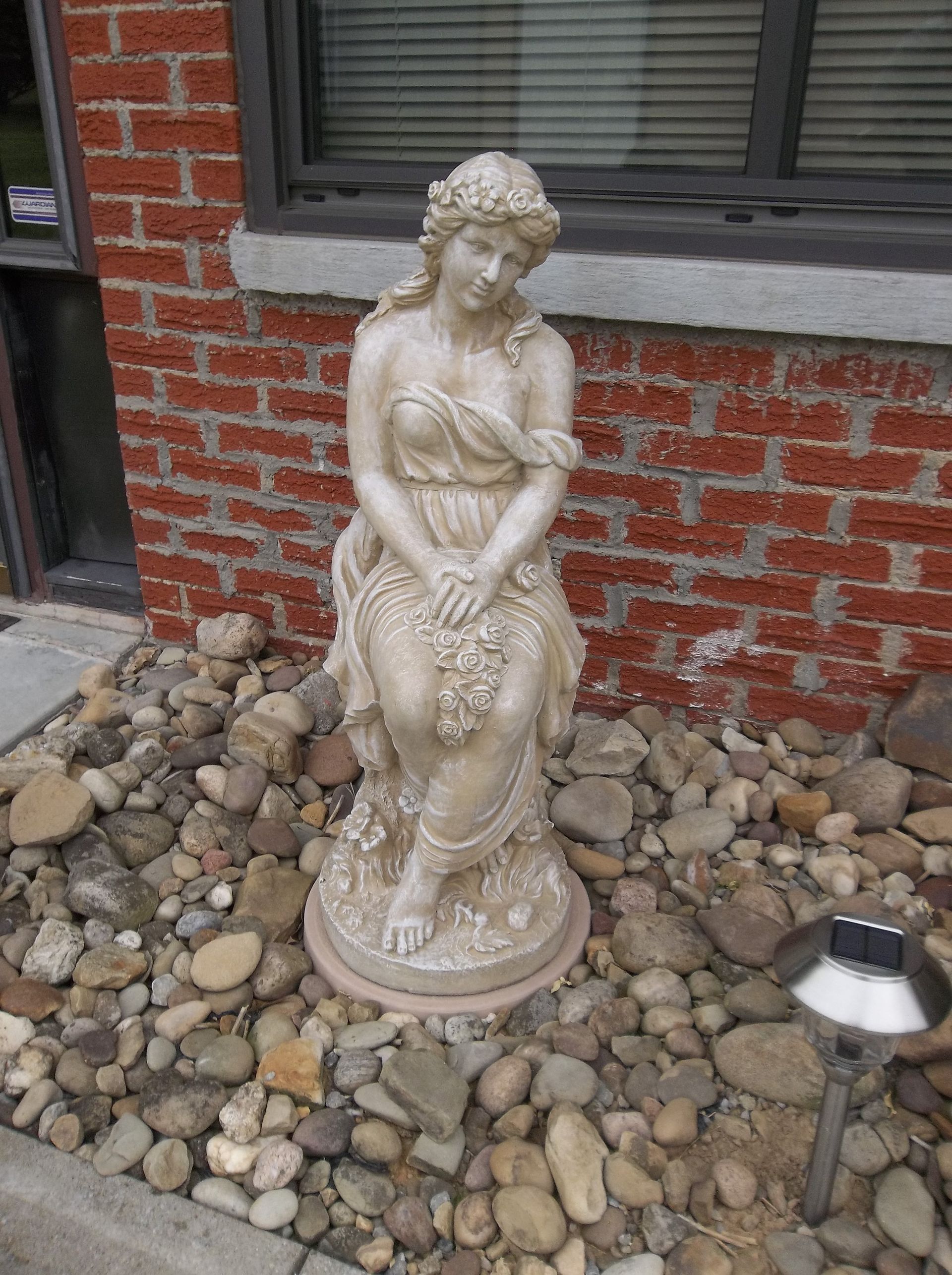 A statue of a woman sitting in front of a brick building