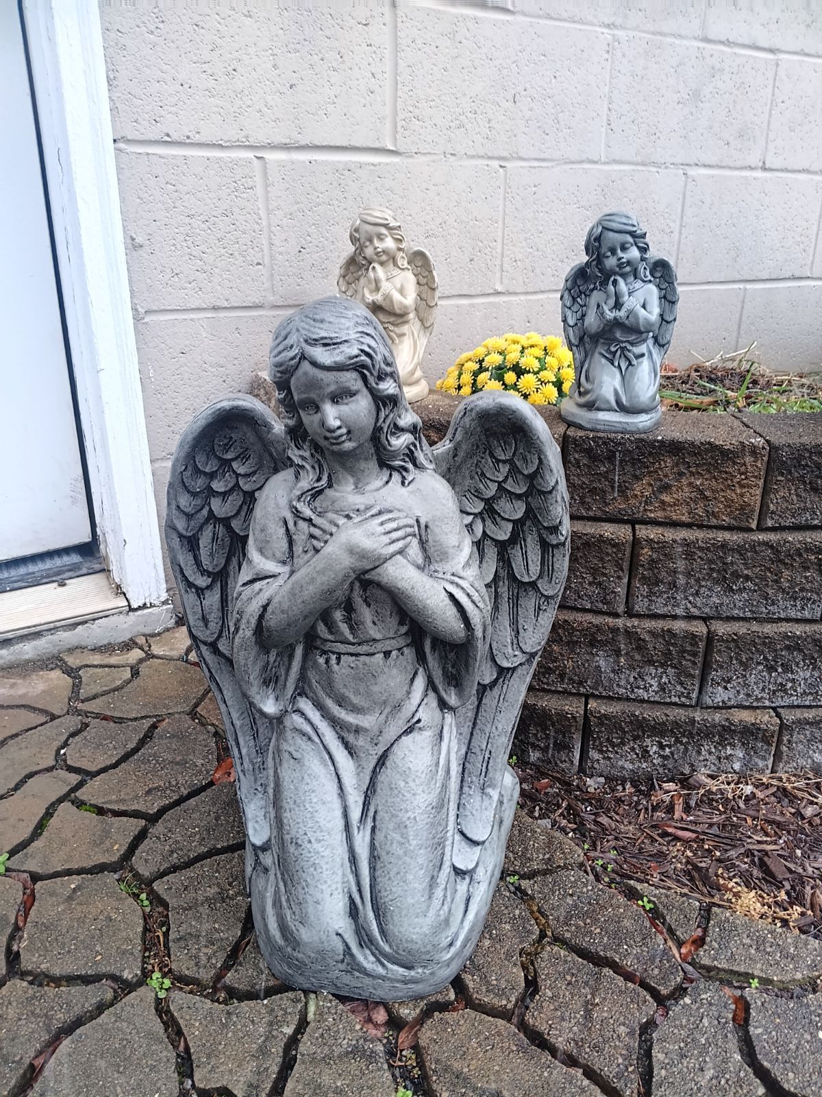 Two statues of angels are sitting on a sidewalk in front of a brick wall.