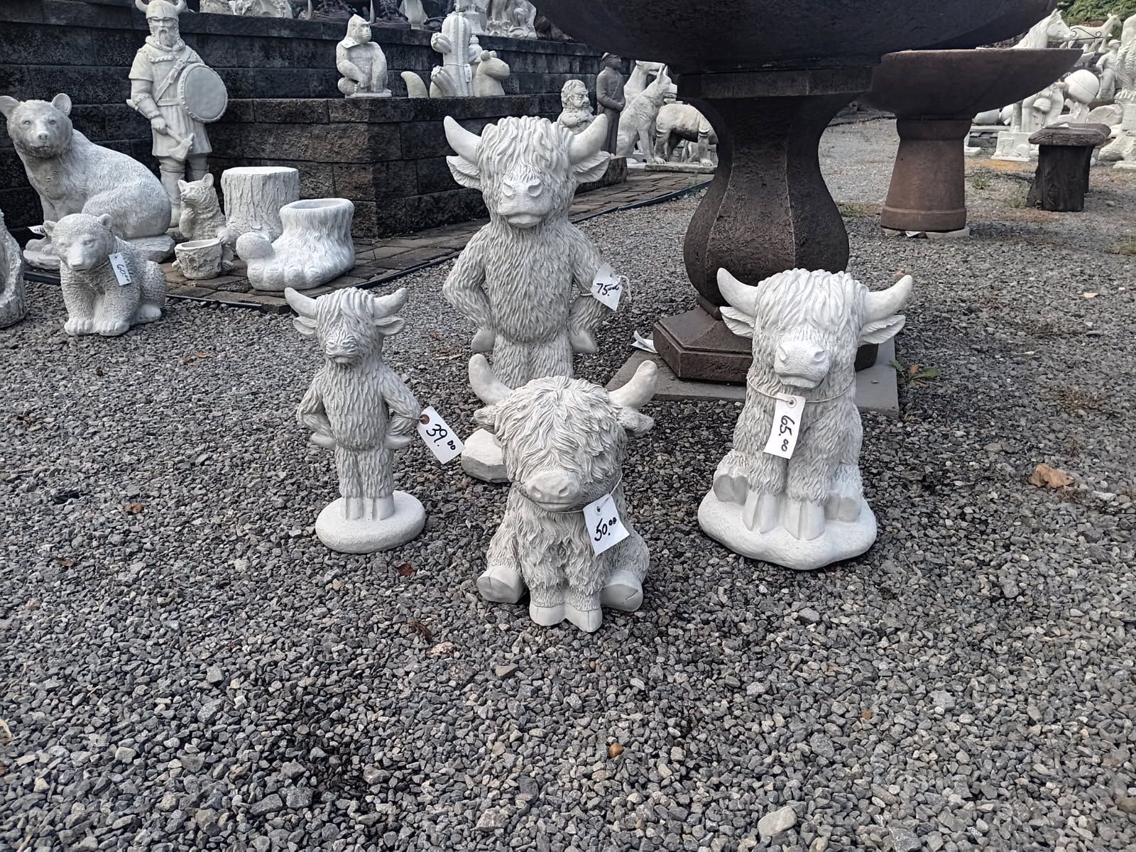 Small stone figurines displayed on gravel in an outdoor garden market.