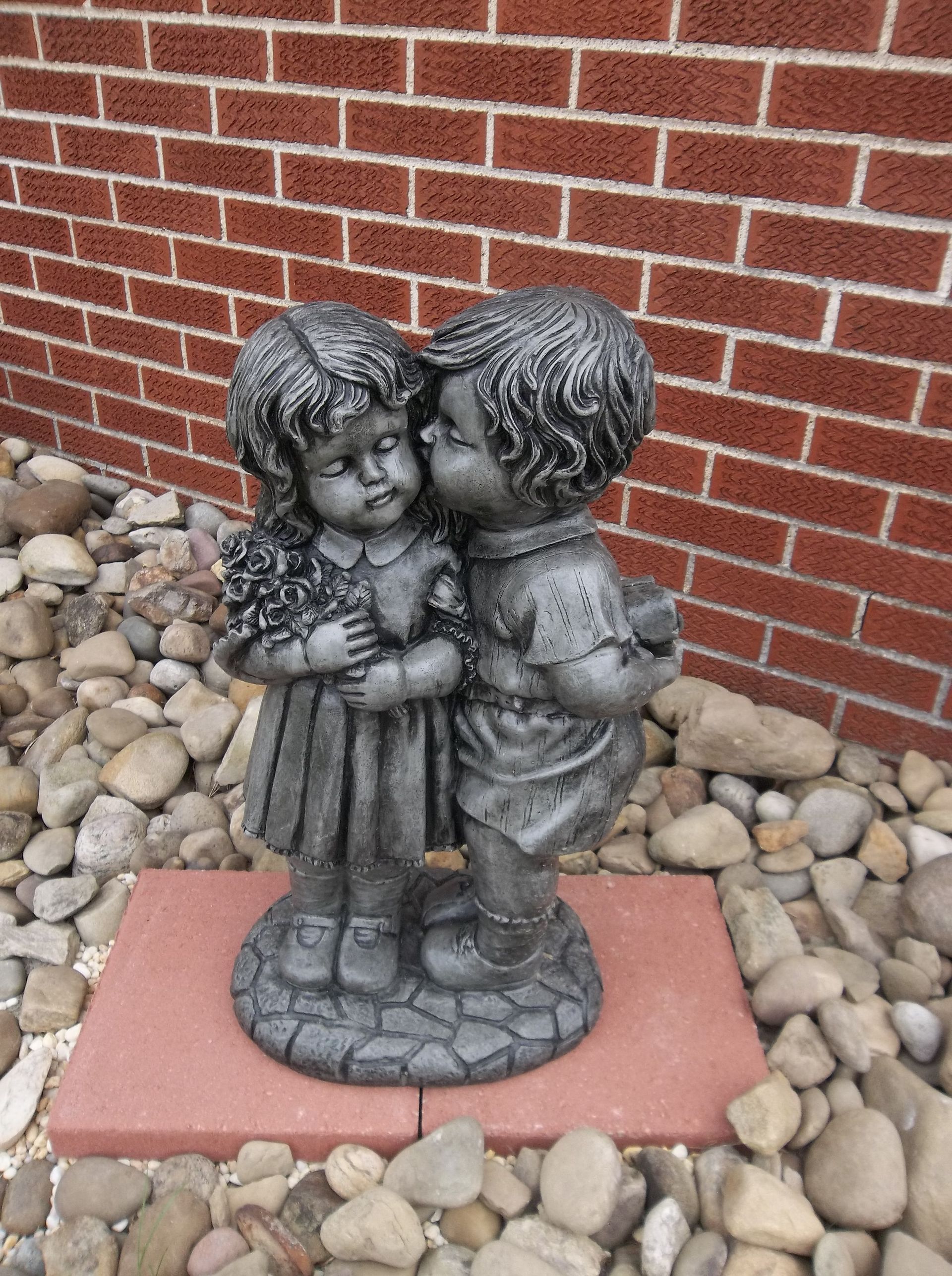 A statue of a boy and girl kissing in front of a brick wall