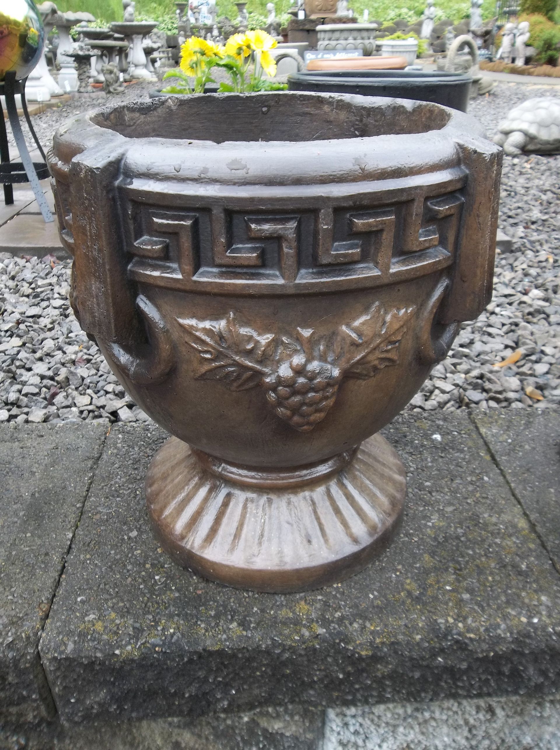 Bronze planter with Greek key design and grape vine detail, sitting on a stone surface.