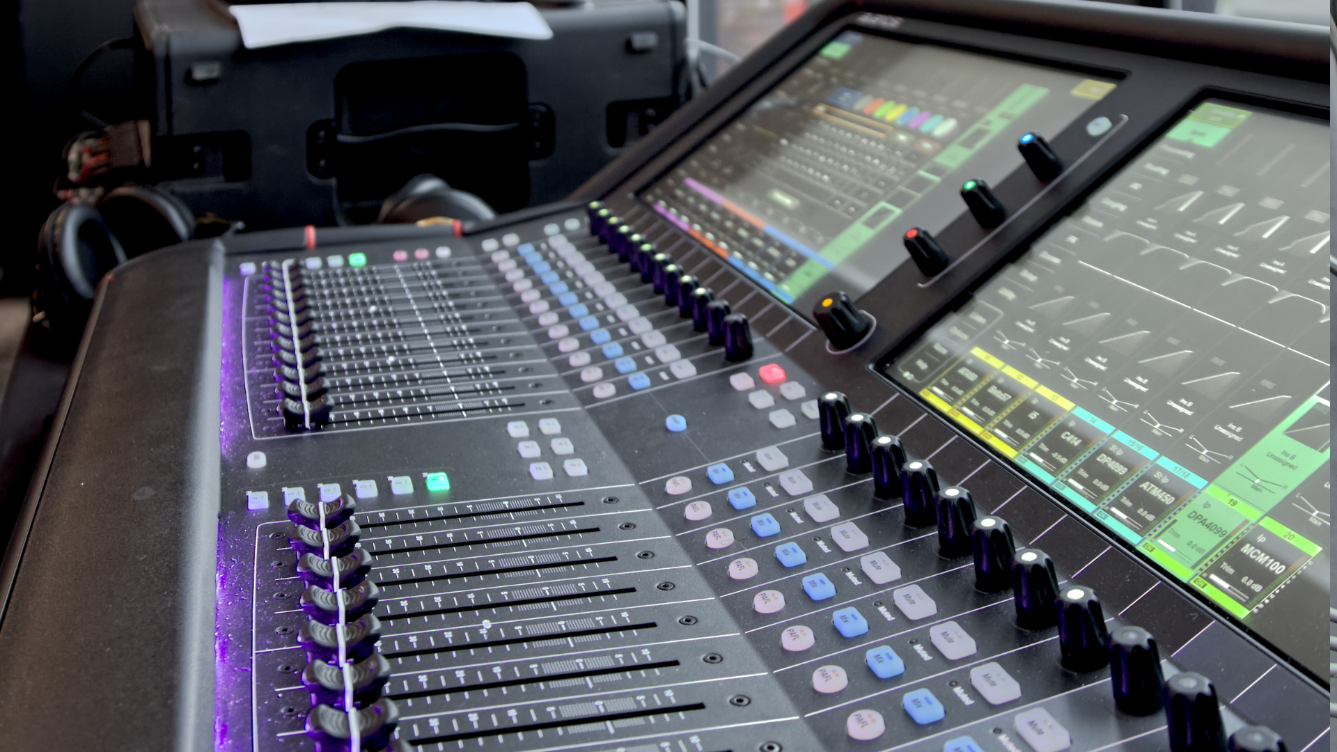 Digital audio mixing console with sliders, knobs, and illuminated touchscreen displays