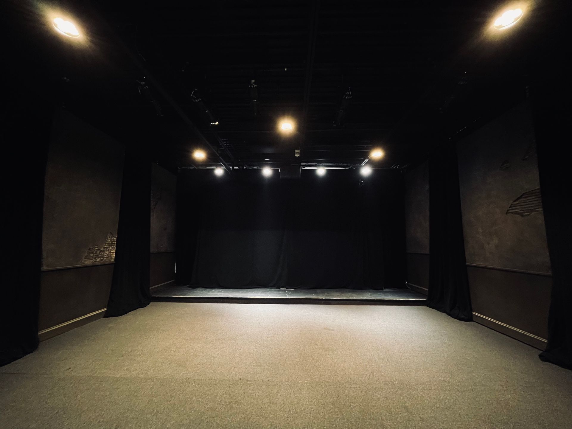 An empty theatre with a black curtain and lights on the stage.