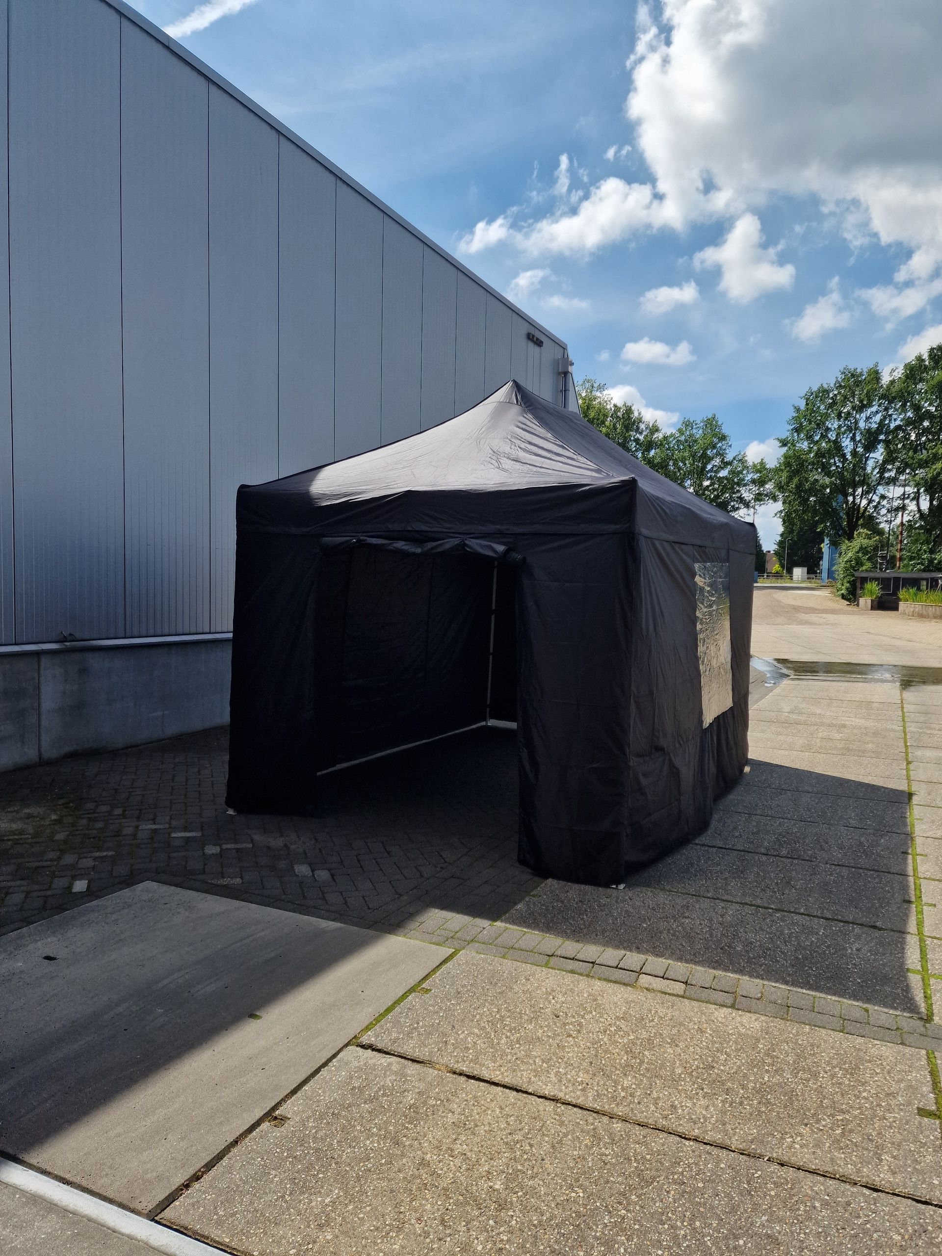 Een zwarte tent staat op een parkeerplaats voor een gebouw.