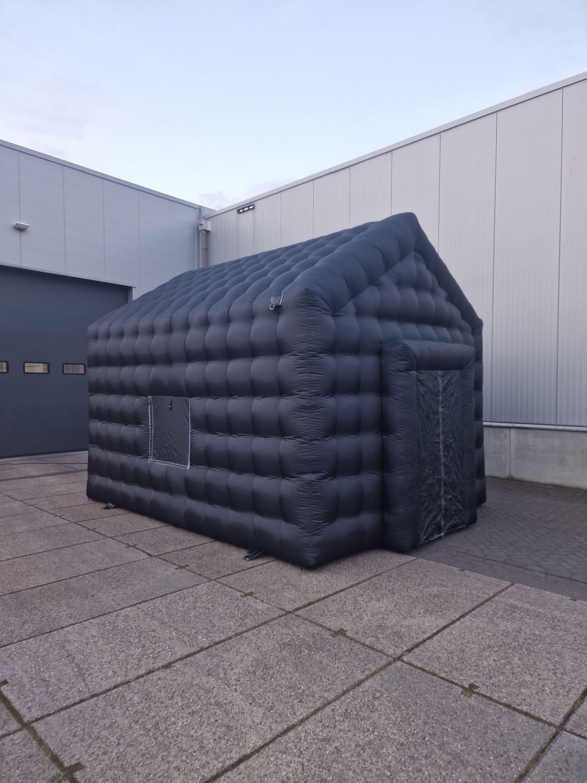 Een groot zwart opblaasbaar huis staat voor een gebouw.