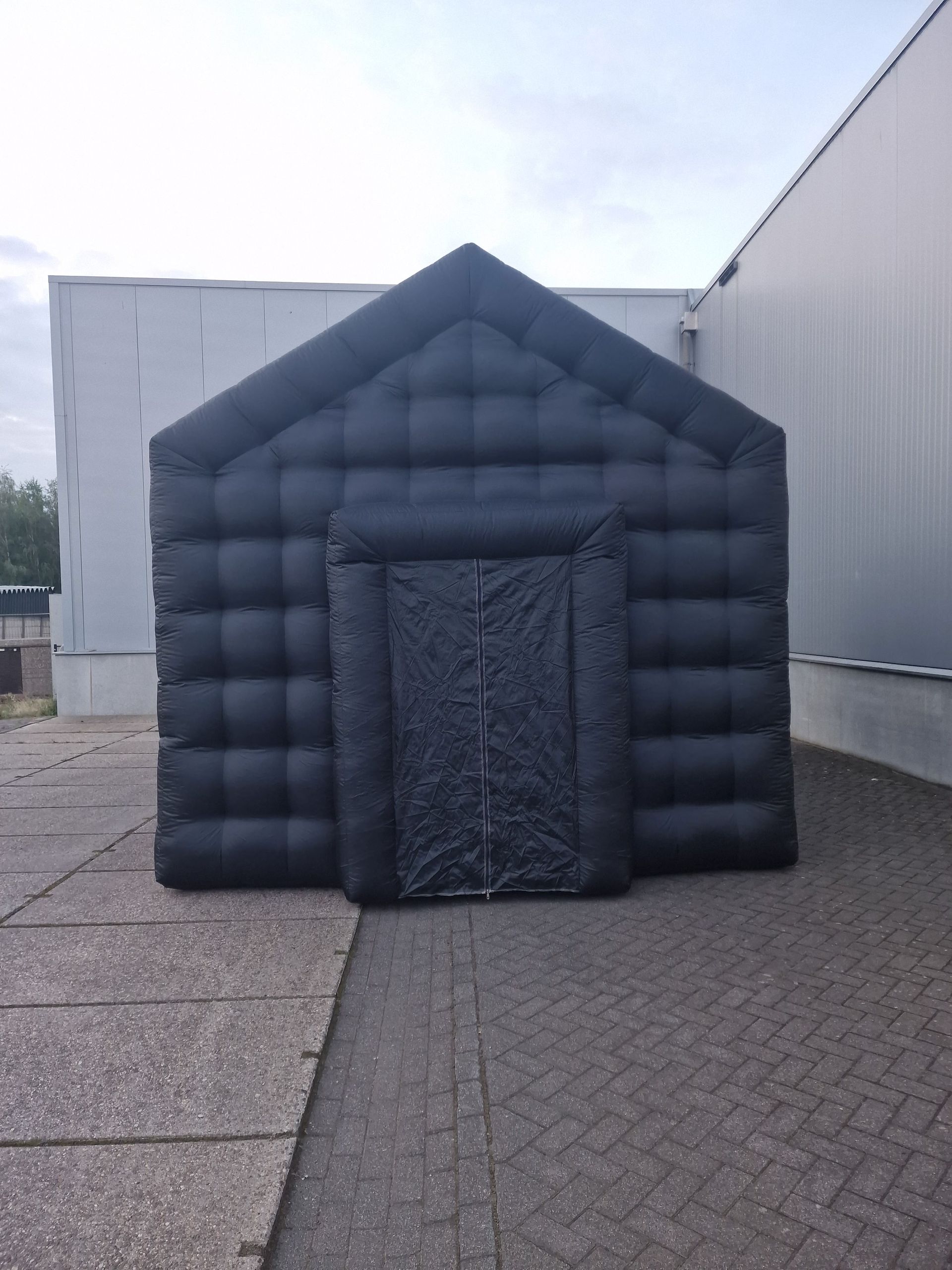 Een groot zwart opblaasbaar huis staat voor een gebouw.