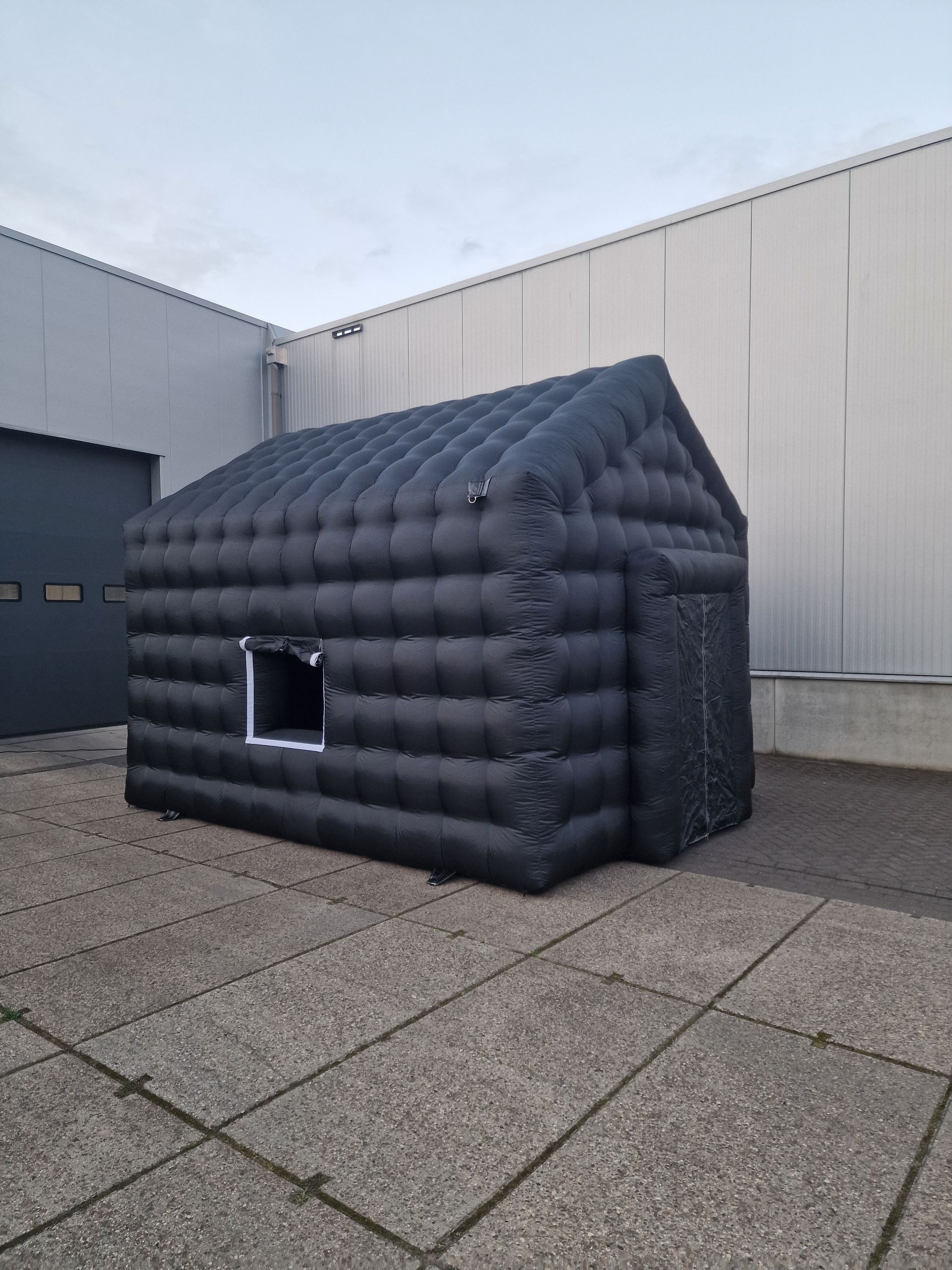 Een zwart opblaasbaar huis staat op een betegelde vloer voor een gebouw.