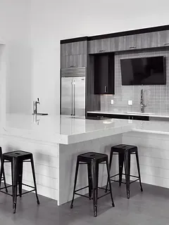 A black and white photo of a kitchen with stools and a large island.