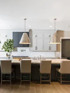 A kitchen with white cabinets , a large island , chairs and pendant lights.