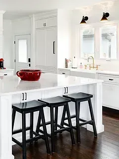 A kitchen with white cabinets , black stools and a large island.