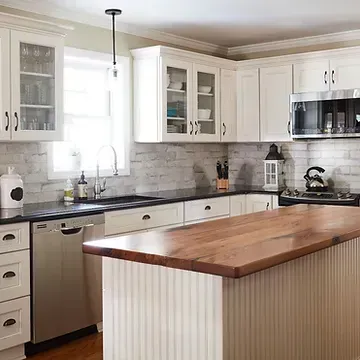 A kitchen with white cabinets , stainless steel appliances , a wooden counter top and a large island.