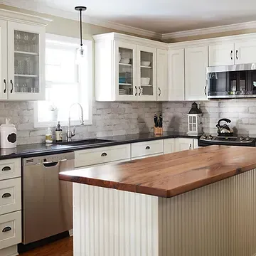 A kitchen with white cabinets , stainless steel appliances , a wooden counter top and a large island.