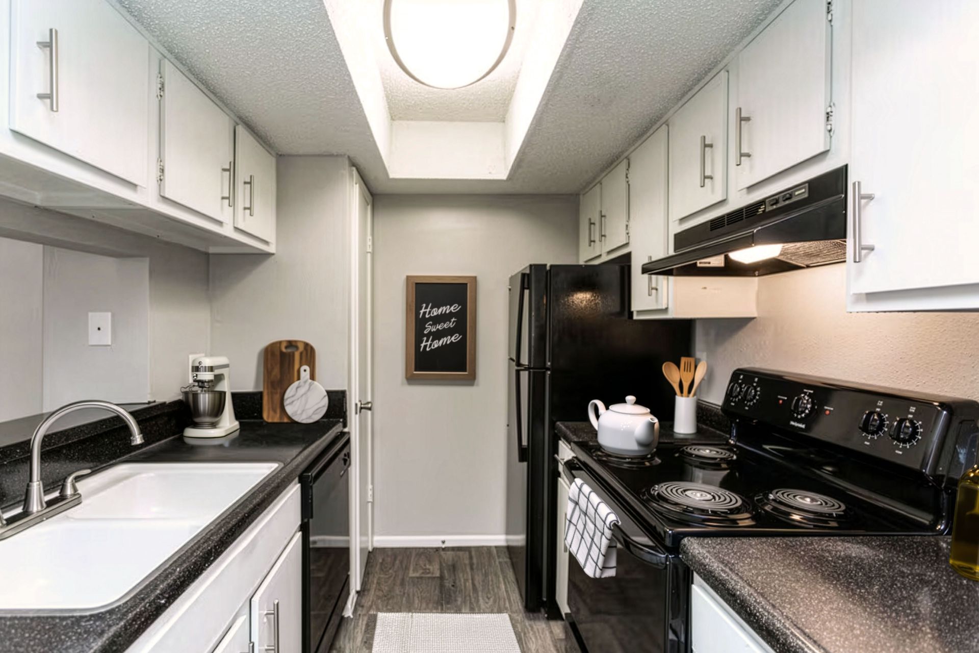 Narrow galley kitchen with white cabinets, black appliances, and a skylight ceiling light