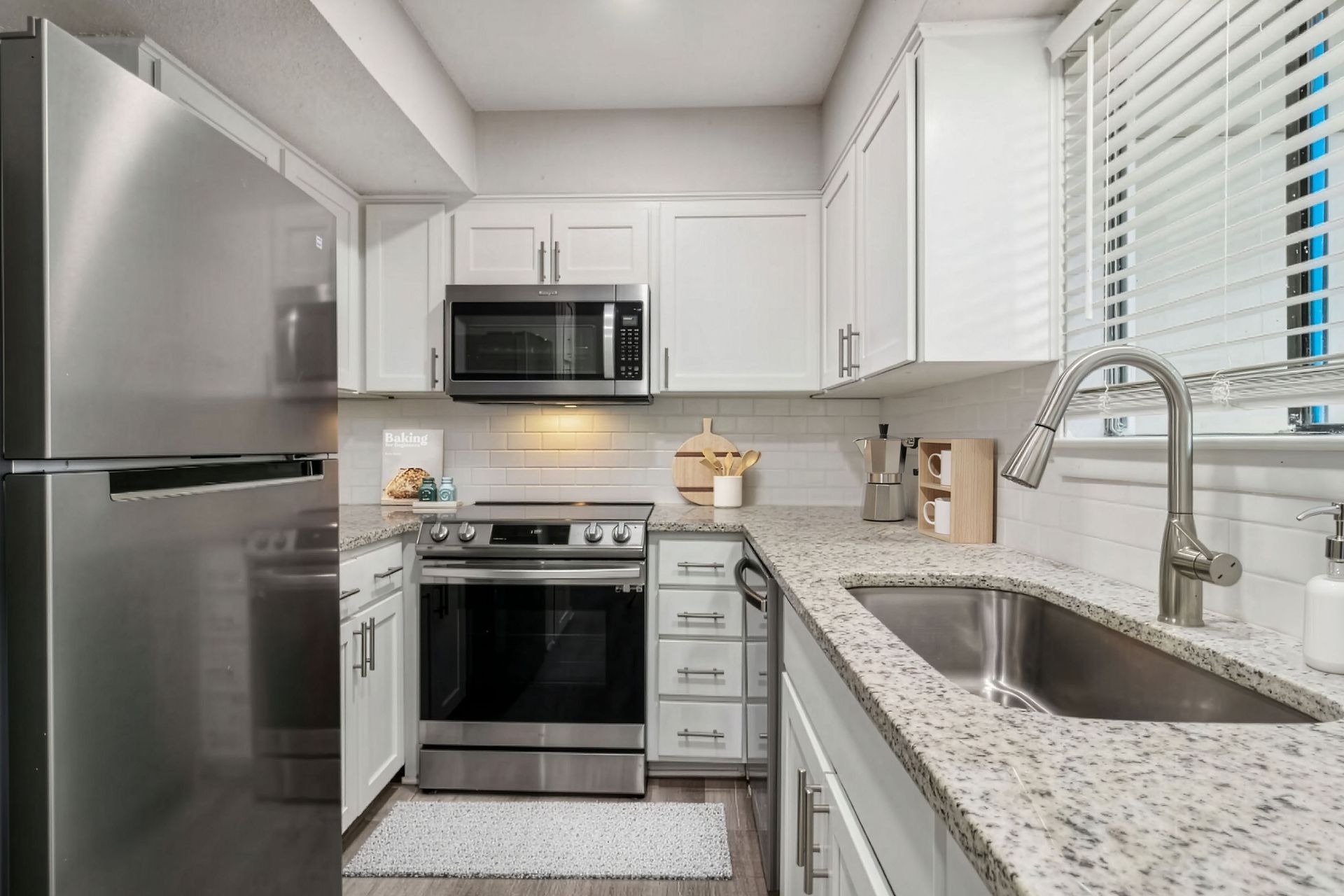 Bright modern kitchen with stainless steel appliances, white cabinets, and a granite countertop with sink.