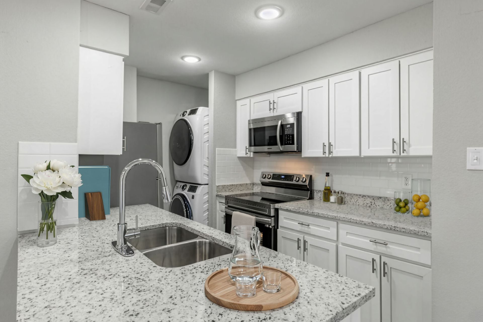 Bright modern kitchen with white cabinets, granite island, stainless appliances, and double sink