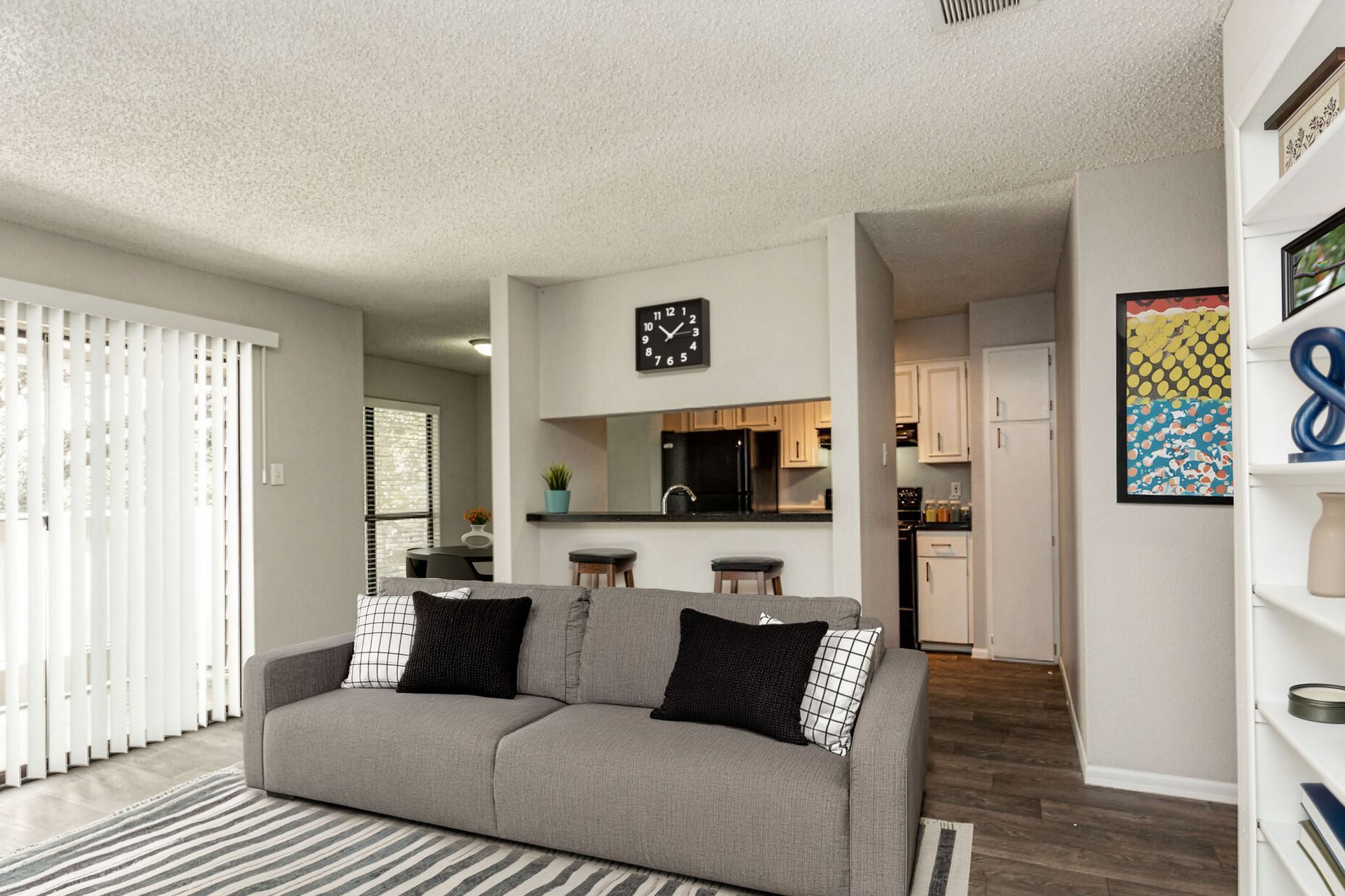 Bright living room with gray sofa, striped rug, wall art, and open kitchen pass-through.