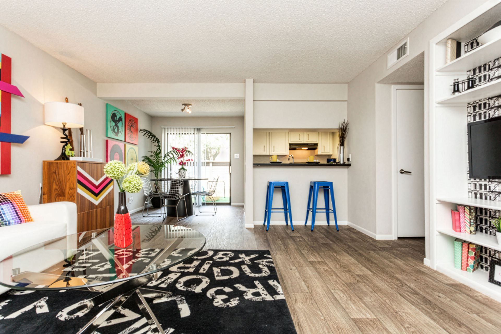 Bright modern living room with black patterned rug, colorful decor, blue stools, and open kitchen area