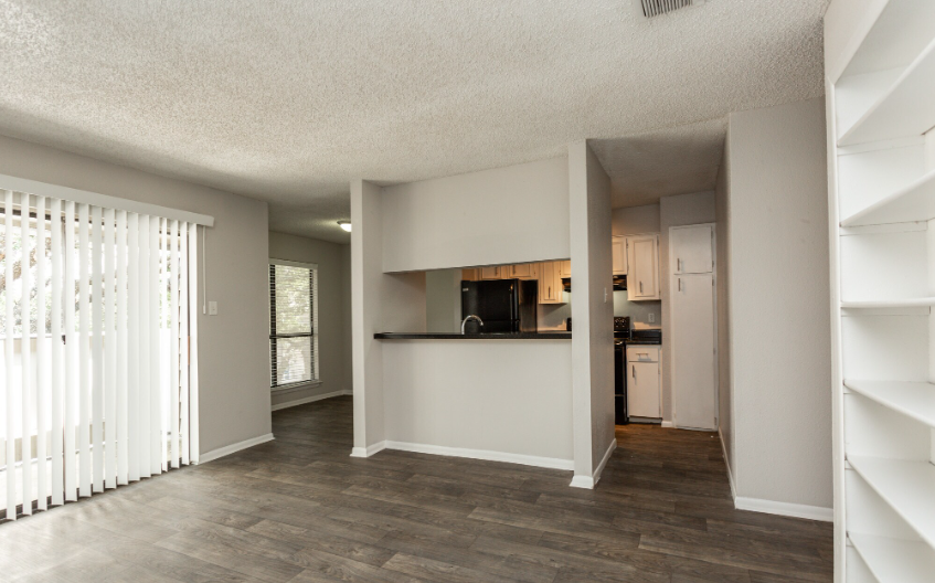 Empty modern apartment living room with wood floors, white walls, and a kitchen pass-through.