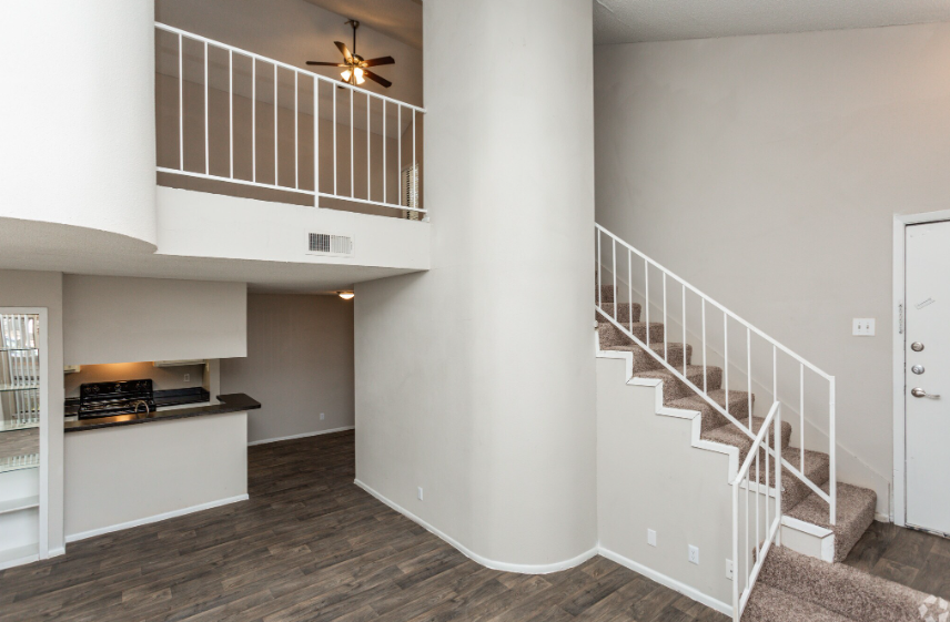 Empty apartment interior with stairs, loft railing, and dark wood flooring