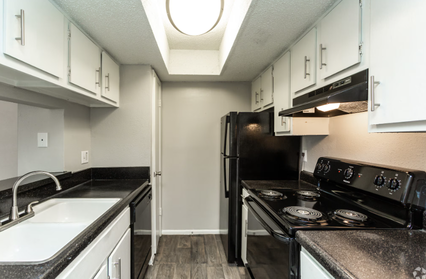Narrow white kitchen with black appliances, counters, cabinets, and a skylight overhead